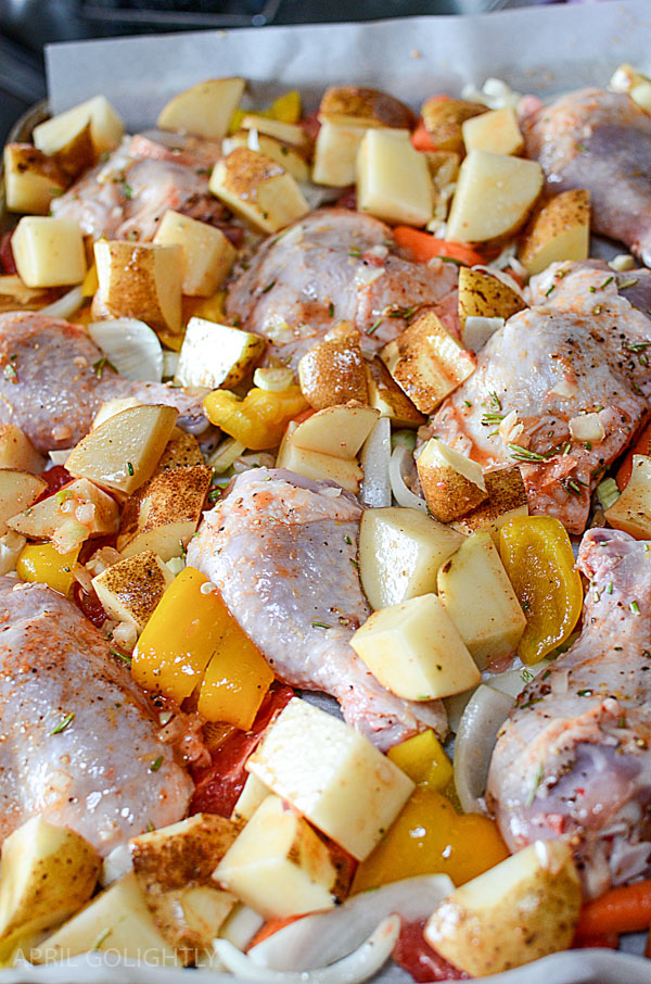Raw chicken thighs on a sheet pan with potatoes and carrots