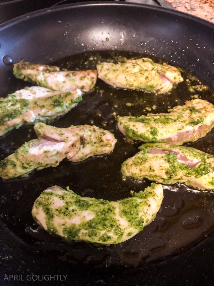 Frying chicken in a skillet with pesto